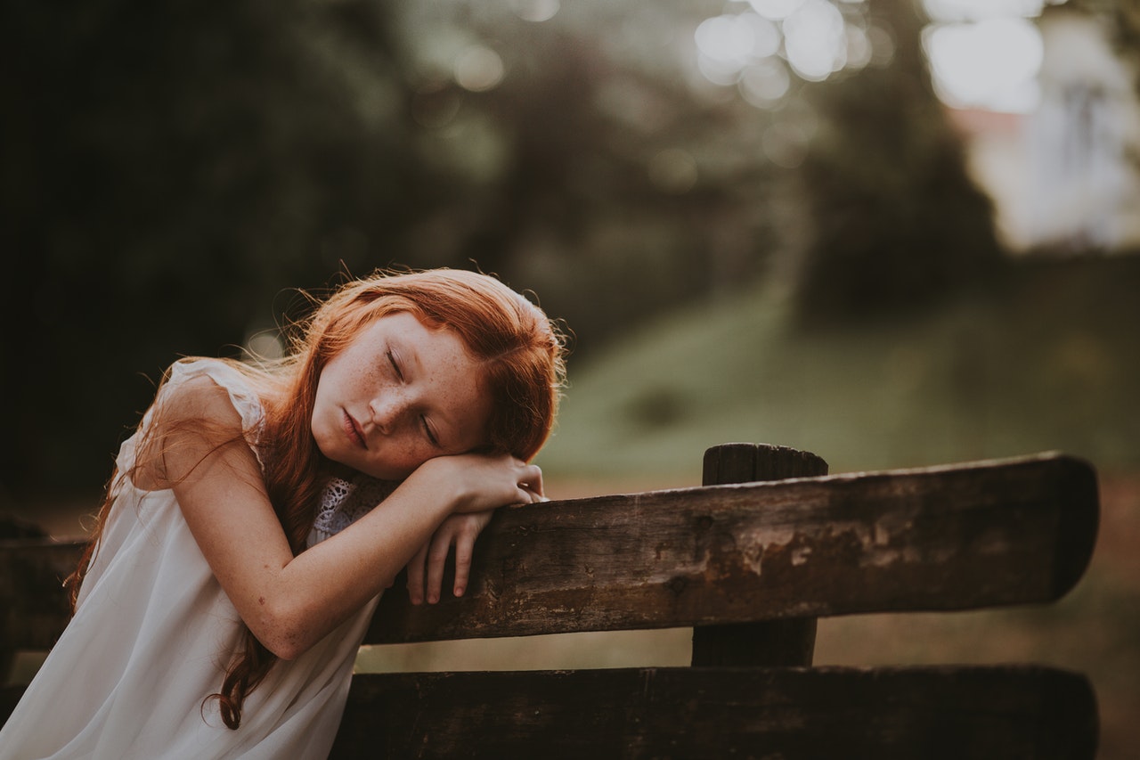 A young girl rest her head on an old wooden fence